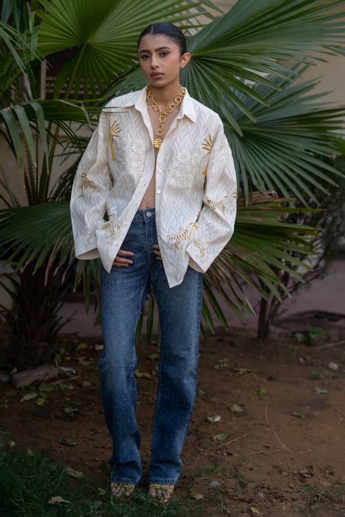 The image displays a woman wearing a jacquard hand-block printed, oversized shirt in white with high-waisted blue jeans. Copyright House of Mae.