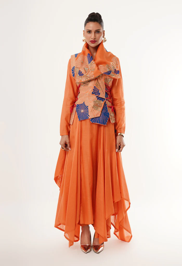 The image displays a woman wearing an orange embroidered Angrakha jacket with an asymmetrical inner kurta and pants. Copyright Jajaabor.