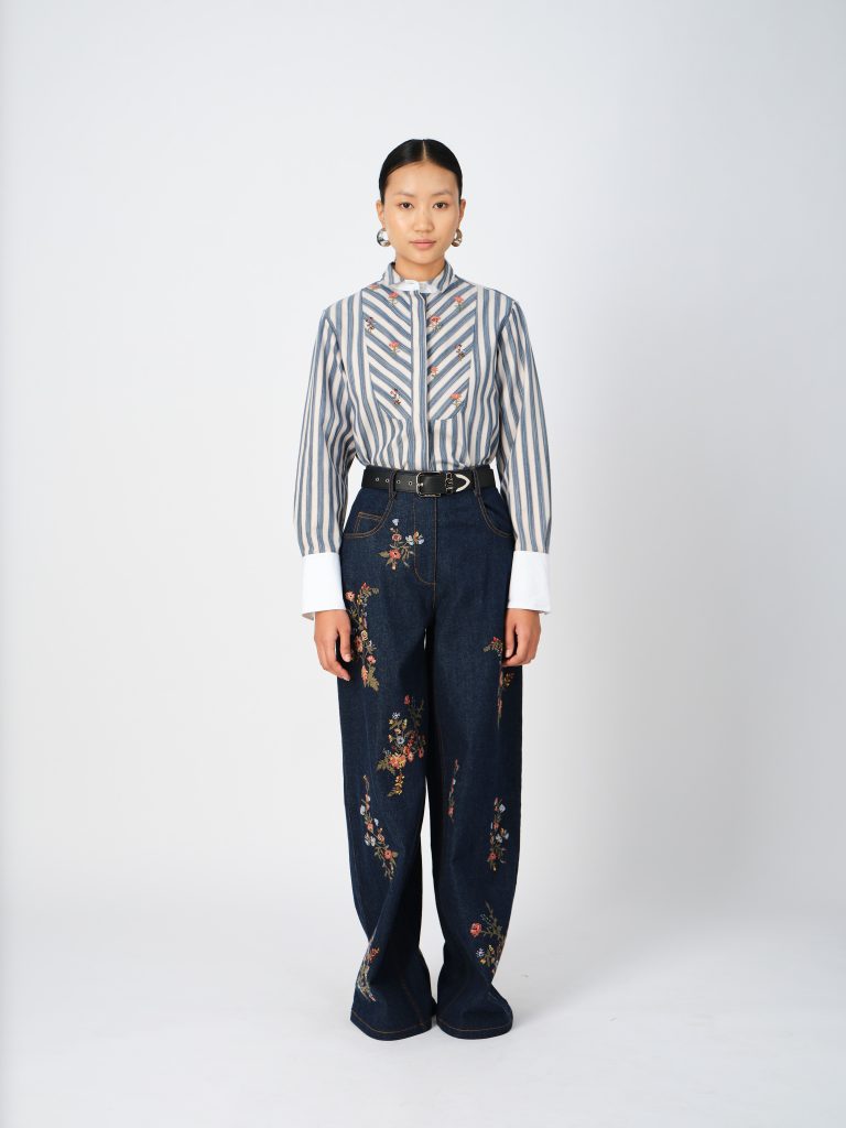 The image displays a woman wearing a shirt that features a yoke panel and handcrafted crystal tassel fringes, as well as cross-stitch denim pants, showcasing vintage-inspired floral hand embroidery. Copyright moonray.
