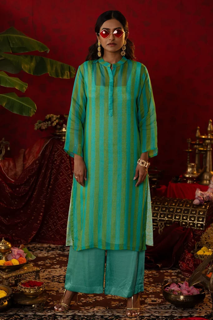 The image displays a woman wearing a Chinese collar kurta with an ajrakh inner paired with straight pants in green and blue. Copyright Pooja Bagaria.