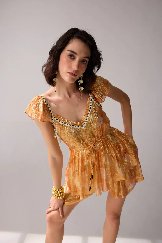 The image displays a woman wearing an orange blouse and shorts co-ord set. Copyright Verb by Pallavi Singhee.