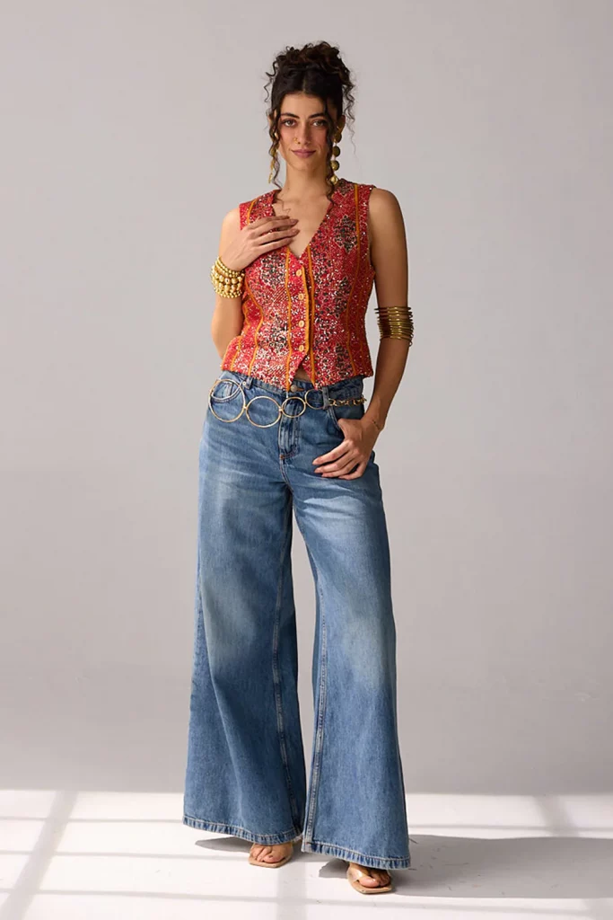 The image displays a woman wearing a red hand-embroidered sequin vest and high-waisted wide-leg jeans. Copyright Verb by Pallavi Singhee.
