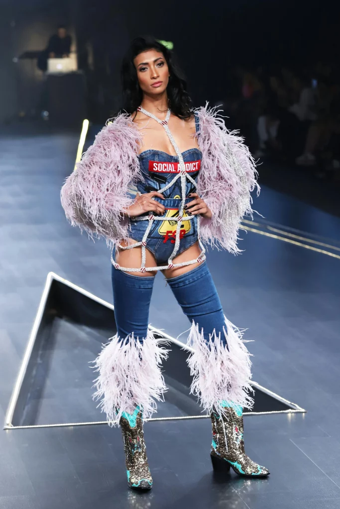 The image displays a woman wearing a feather jacket, denim bodysuit, cowboy boots, and sparkly jewelry. Copyright Rajesh Kumar Verma/Pexels.